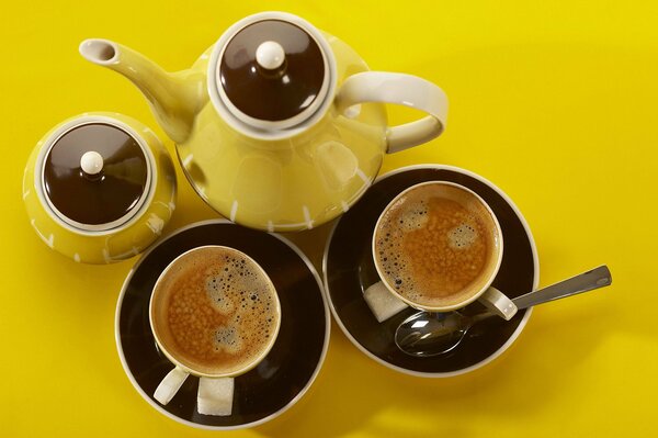 Two mugs of coffee with a kettle on a yellow table