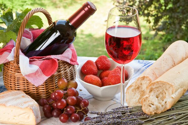 Baguette, strawberries, grapes, a glass of red wine in nature