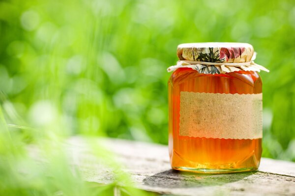 Delicious jar of honey on a wooden table surrounded by green foliage