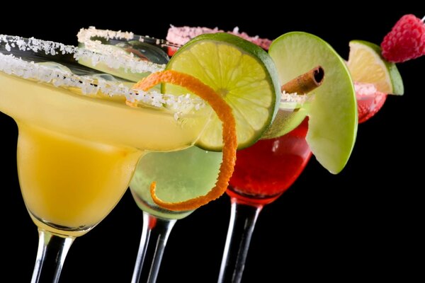 Bokabs with cocktails framed by a sugar border on the sides of glasses with decorations of orange peel, lime slice, cinnamon stick, apple, and raspberry on a black background