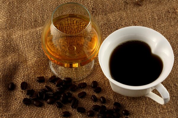 A cup of coffee, a glass of cognac and scattered coffee beans on a jute cloth