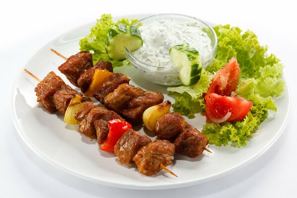 Shish kebab avec légumes, herbes et sauce sur une plaque blanche