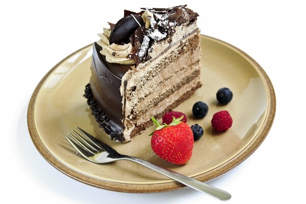 A piece of cake with chocolate icing and cream next to berries, lying on a saucer