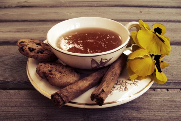 Taza de té con galletas y canela, flores en platillo