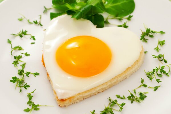 Œuf au plat sur du pain grillé en forme de coeur avec des légumes verts sur une assiette