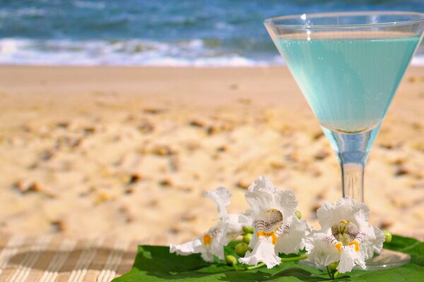 Ein Glas mit einem Getränk und Blumen auf dem Hintergrund des Strandes am Meer