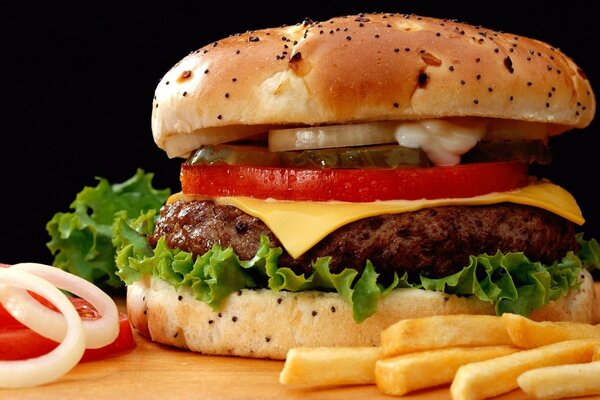 Hamburger con cotoletta, formaggio, verdure ed erbe, ghiaccio su una tavola tra verdure e patatine fritte