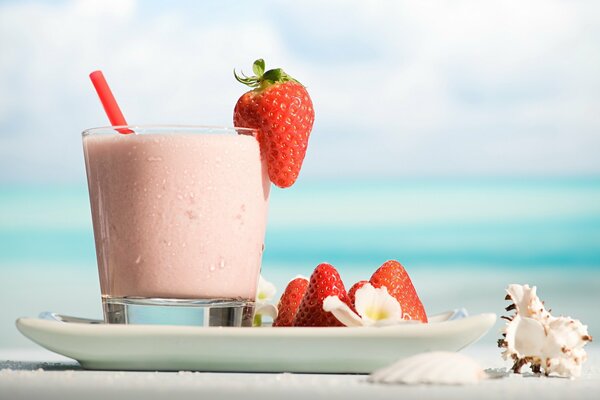 Strawberry cocktail surrounded by seashells on the seashore