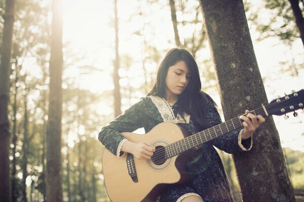 Chica tocando la guitarra en el bosque