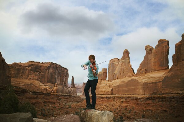 A young man plays the violin against the background of mountains