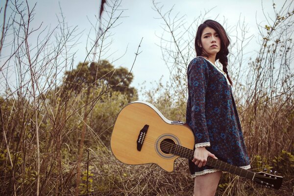 A girl with a guitar on the background of nature