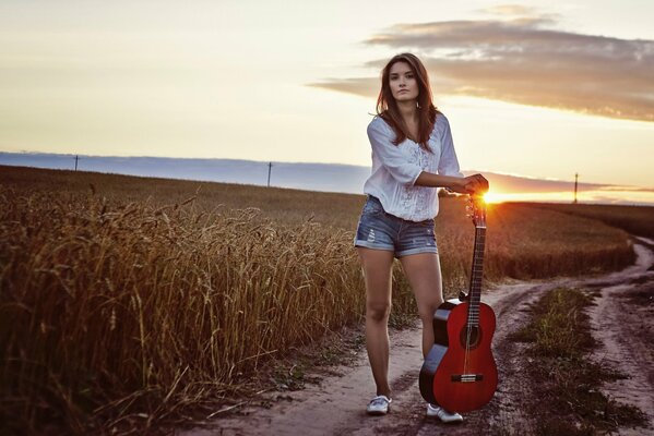 A girl with a guitar in a field on the background of sunset