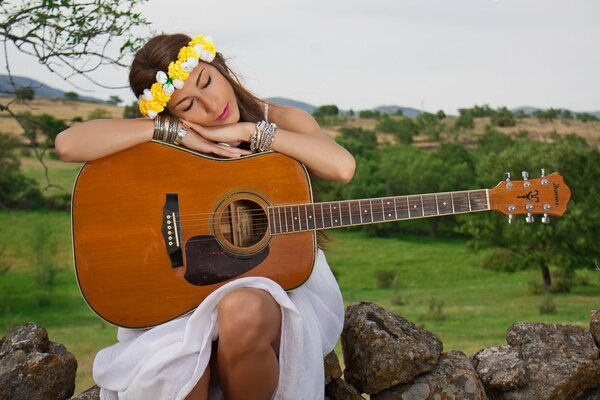 Schönes Mädchen in einem Kranz mit einer Gitarre