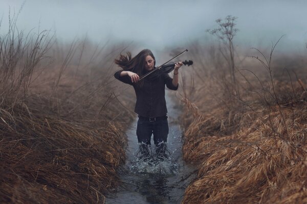 A girl knee-deep in a stream plays the violin