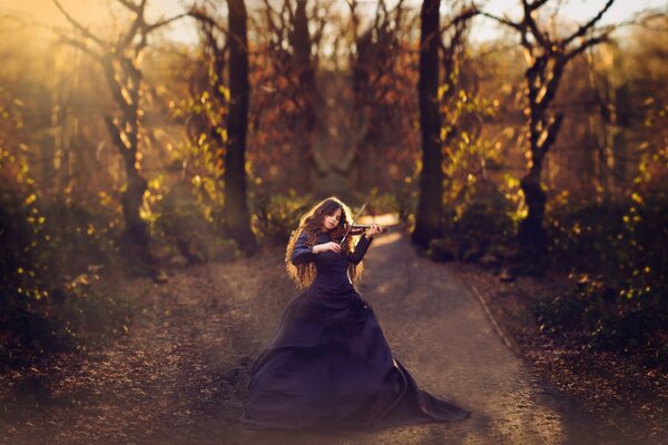 A girl plays the violin in a long dress under the rays of the sun