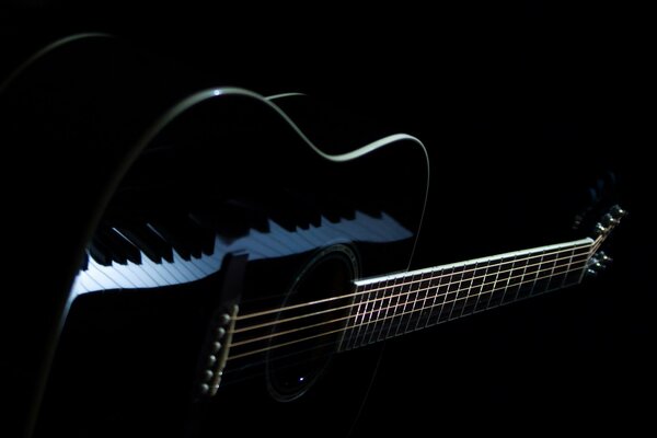 The piano keys are reflected in the black guitar