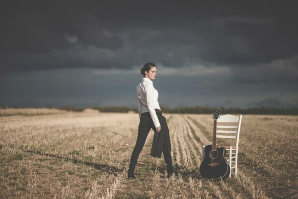 Mädchen im weißen Business-Hemd auf dem Feld mit Gitarre und Stuhl