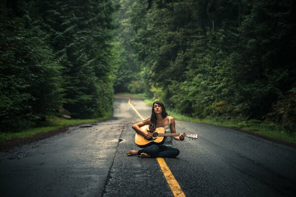 A girl with a guitar is sitting in the middle of the road