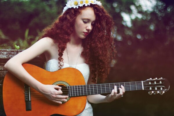 Ein Mädchen in einem Gänseblümchenkranz spielt Gitarre