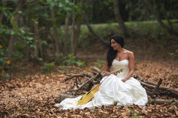 Ragazza in abito da sposa si siede nel bosco con la chitarra