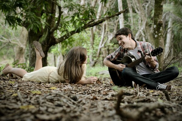 A guy plays a guitar to a girl in the woods