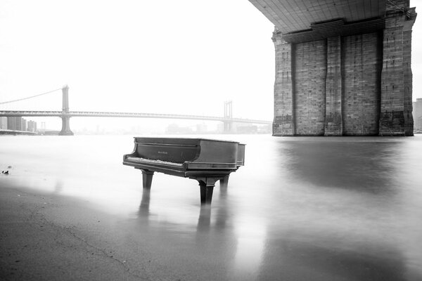 Piano in the river on the background of the bridge in black and white