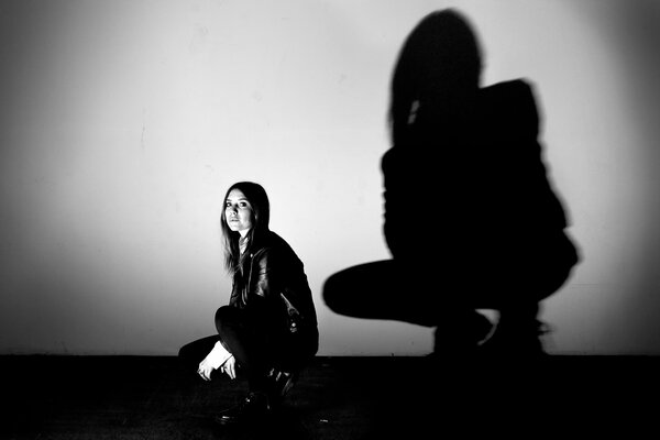 The girl is squatting on a gray background, her black shadow is reflected