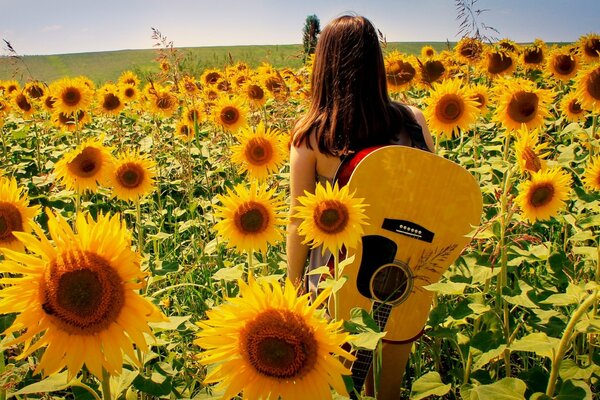 A girl in sunflowers with a guitar stands with her back