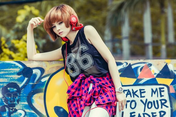 An Asian girl stands and listens to music with headphones