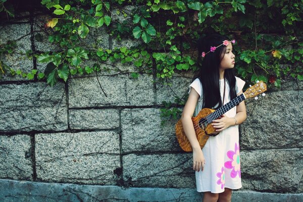 A beautiful girl in a white dress plays music on the guitar