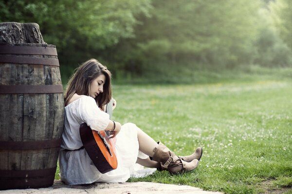 Chica con guitarra sentada cerca de un barril