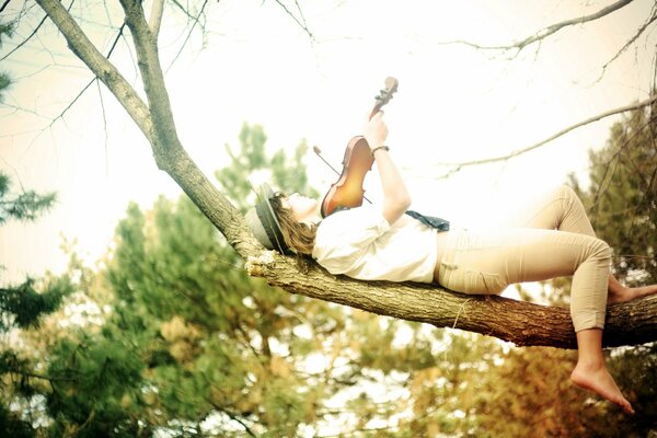 Ragazza sdraiata su un albero con un violino in mano