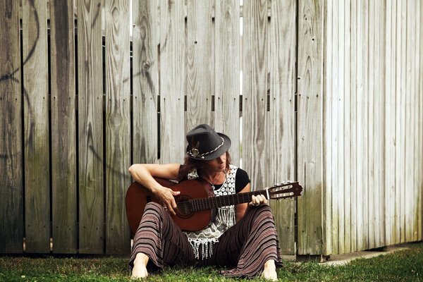 A young guitarist in a hat near the fence