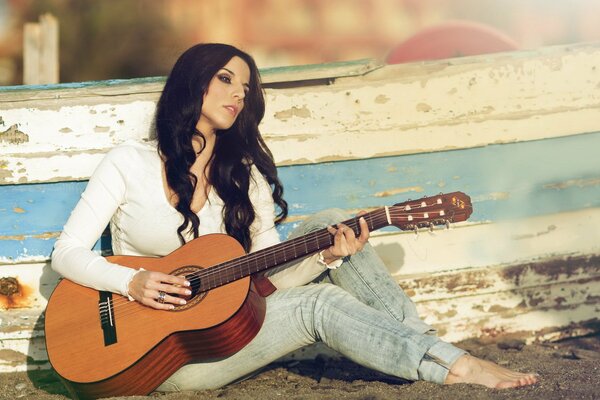 A girl with a guitar is sitting on the sand