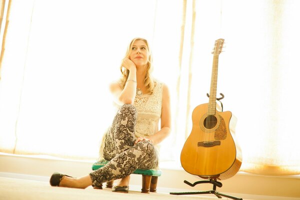 A girl is sitting next to a guitar in a sunny room