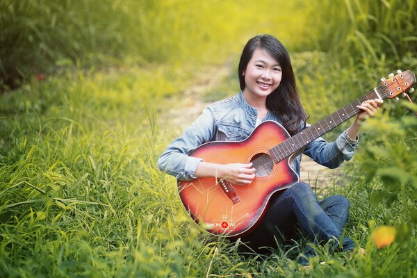 Songs to the guitar on a green meadow Asian girl