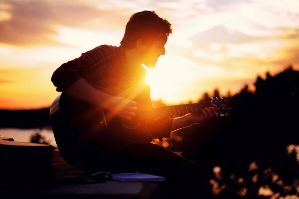 Un gars qui joue de la guitare au coucher du soleil