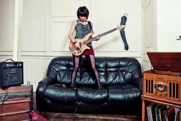 Chica tocando la guitarra eléctrica de pie en el Sofá