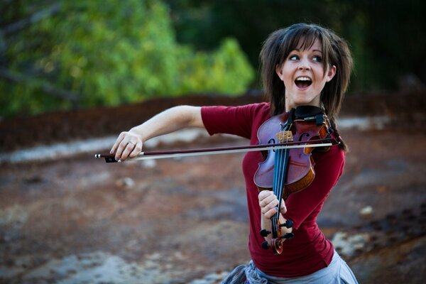 Lindsay Stirling, playing the violin in the background of nature