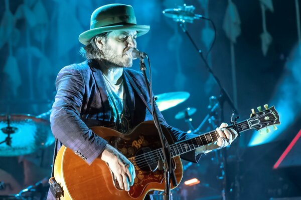 A musician in a hat with a guitar sings at a concert