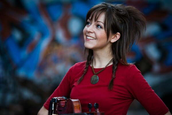 Lindsey Stirling ze skrzypcami przy ścianie z graffiti