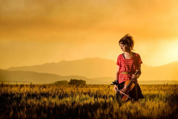 La violinista Lindsay Stirling en un campo en medio de una puesta de sol