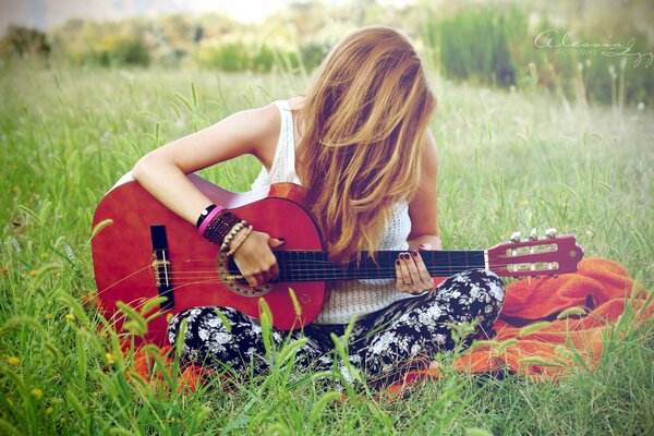 A girl with a guitar is sitting on the grass