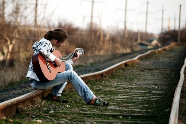 Girl playing guitar sitting on rails