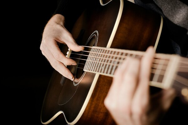 Hände auf den Saiten einer akustischen Gitarre