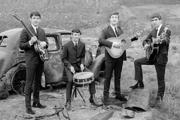 Black and white photo of the Beatles at a rusty car