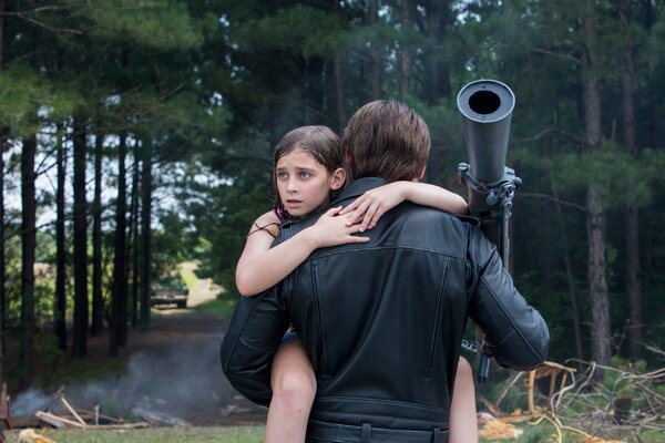 A shot from the movie terminator: genisys, where a man carries a girl in his arms against the background of a forest