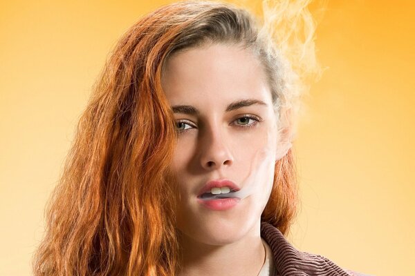 Kristen Stewart with red hair exhales smoke on a yellow background