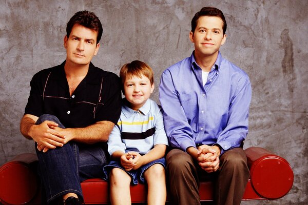 Two guys and a boy are sitting on a red couch