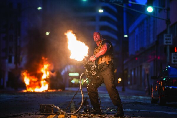 Dwayne Johnson on the street with a gun spewing fire